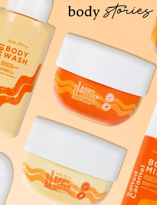A flat-lay product collage of body care items from body stories, including a body wash bottle, a body butter jar, and a body scrub jar, arranged on a peach background with the brand name 'body stories' written at the top.
