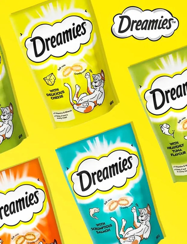 Four bags of Dreamies cat treats arranged diagonally on a bright yellow background. The bags are in different flavor colors: lime green (cheese), orange (salmon), turquoise (salmon), and light green (tuna).