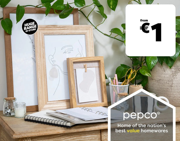Three framed minimalist art prints in light wood frames displayed on a wooden desk alongside a notebook, pen cup, and houseplant. A black circular sticker reads 'HUGE RANGE OF STYLES' and a white promotional badge says 'from €1'.